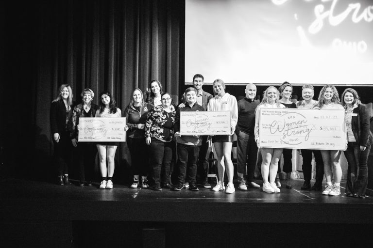Group of people standing on stage holding large checks