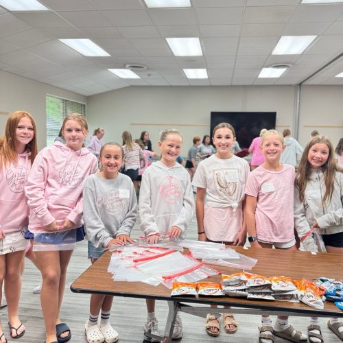 Group of girls wearing 100 Girls Strong hoodies helping to pack snack bags for charity
